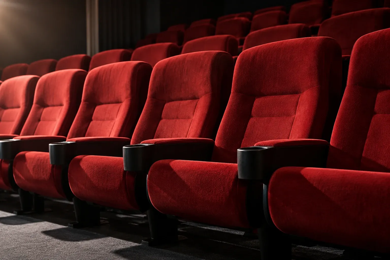 Fila de butacas rojas acolchadas en sala de cine vacía con posavasos negros